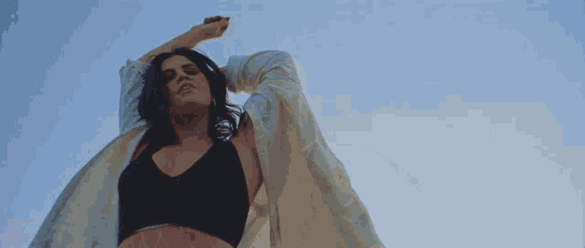 a woman in a black bra and white shirt is standing in front of a blue sky with her arms outstretched