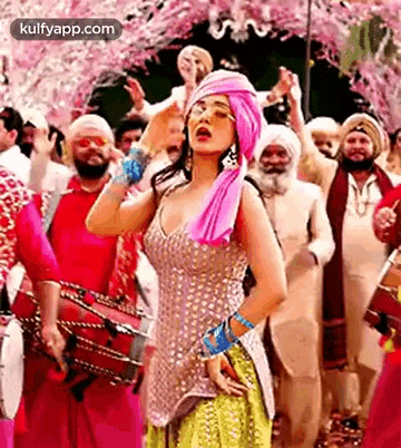 a woman in a turban is dancing in front of a group of men playing drums .