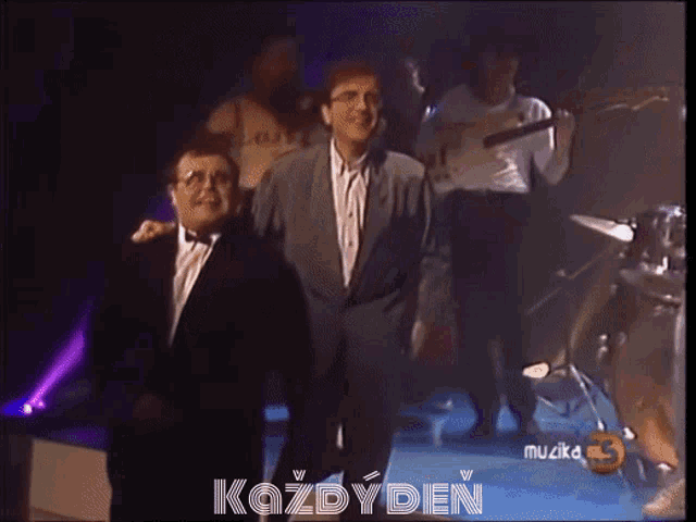 a group of men standing on a stage with the words kazdyden on the bottom right