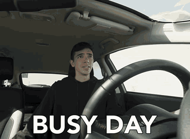 a man is sitting in a car with the words busy day written above him