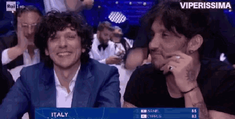 two men are sitting in front of a screen that says italy on it
