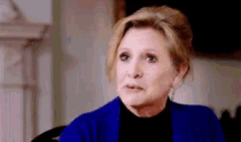 a woman in a blue jacket is sitting in a chair making a funny face .