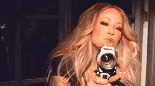 a woman is holding a camera and blowing a kiss