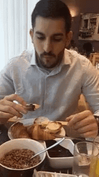 a man is sitting at a table with a bowl of cereal and a plate of food .