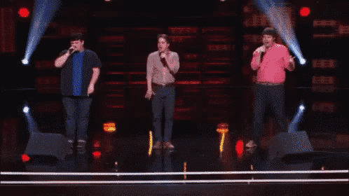 three men are standing on a stage with one raising his fist in the air