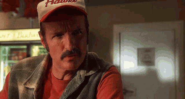 a man with a mustache wearing a hawks hat