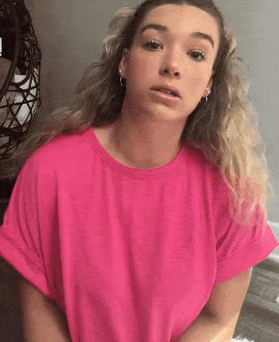 a woman wearing a pink t-shirt and hoop earrings looks at the camera