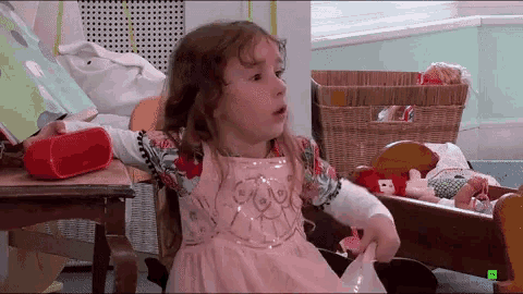a little girl in a pink dress is sitting on a rocking chair in front of a book and a red speaker