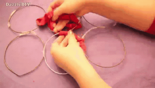 a person is making a headband out of wire and a red flower .