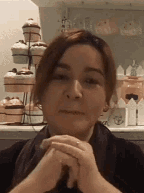 a woman with her hands folded in front of a display of cupcakes
