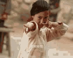 a young girl is pointing at the camera with her arms outstretched in a karate pose .