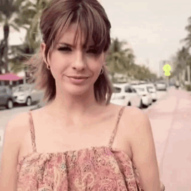 a woman in a pink dress is walking down a sidewalk and smiling .
