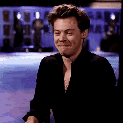 harry styles is making a funny face while wearing a black shirt and necklace .
