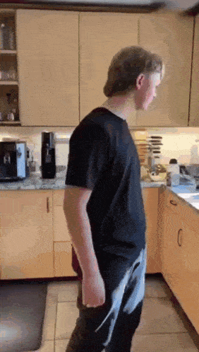 a man in a black shirt is standing in a kitchen holding a knife