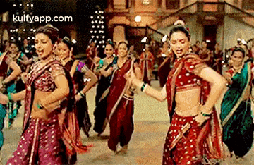 a group of women in traditional indian clothing are dancing in a line .