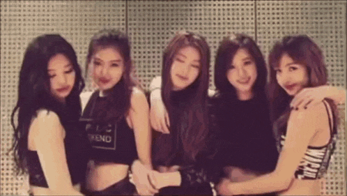 a group of young women are hugging each other in front of a wall with holes in it .