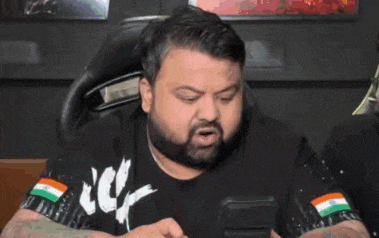 a man with a beard is sticking his tongue out while looking at a cell phone .