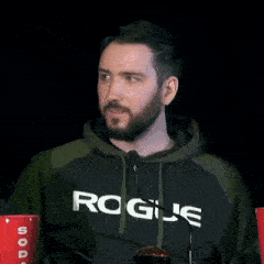 a man with a beard wearing a rogue hoodie is making a funny face .