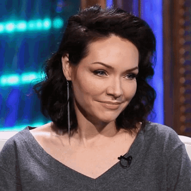 a woman wearing a grey sweater and earrings is smiling