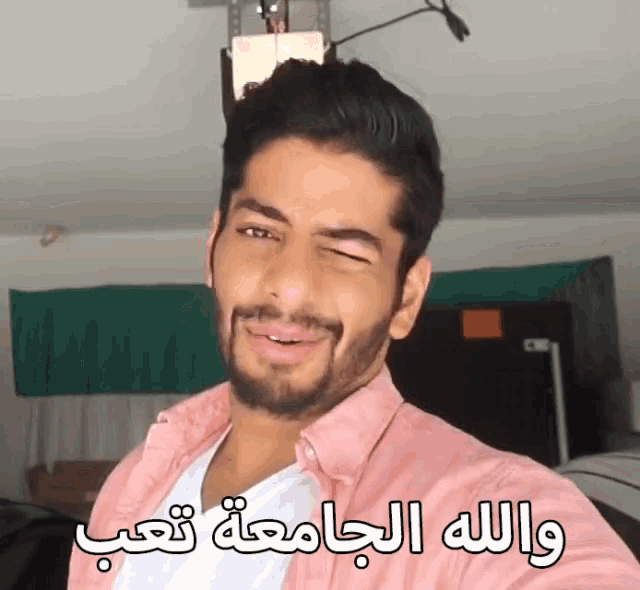 a man in a pink shirt is making a funny face with arabic writing behind him