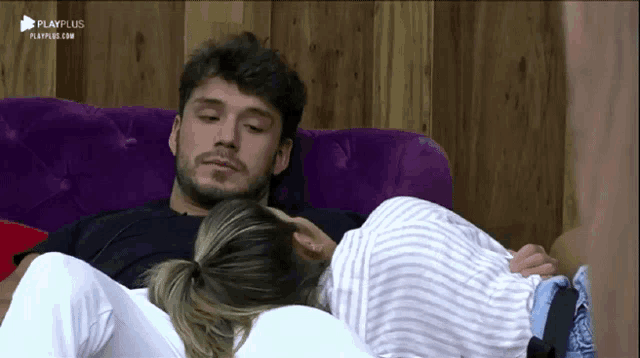 a man and a woman are laying on a purple couch with playplus written on the bottom of the screen