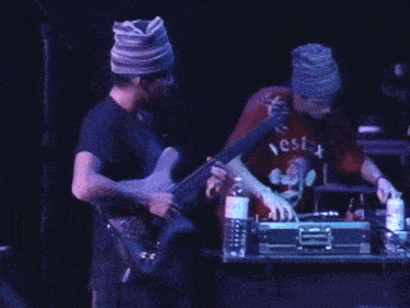 a man wearing a vestax shirt is playing a bass guitar