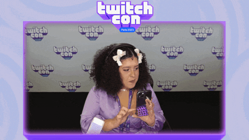 a woman is looking at her phone in front of a twitch con background