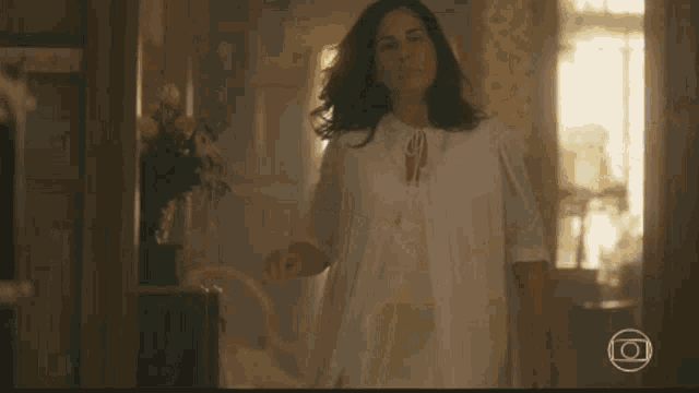 a woman in a white dress is standing in a room with a picture of a camera in the corner