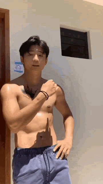 a shirtless man with a tattoo on his chest stands in front of a white wall .