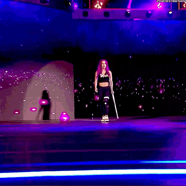 a woman walking on a stage with a crutch and a purple background