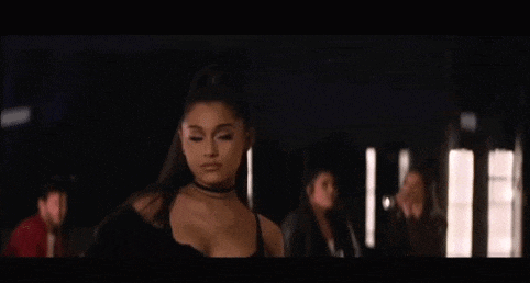 ariana grande is standing in a dark room wearing a choker necklace and a black top .