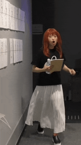 a woman with red hair is standing in a hallway holding a clipboard and a water bottle .
