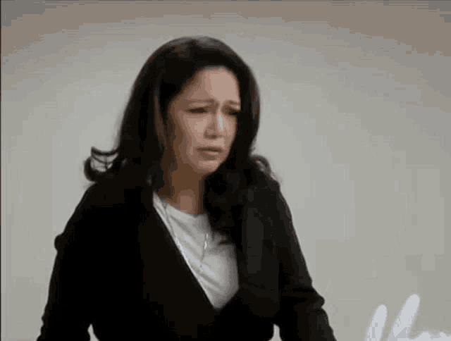 a woman in a black jacket is crying while standing in front of a wall .
