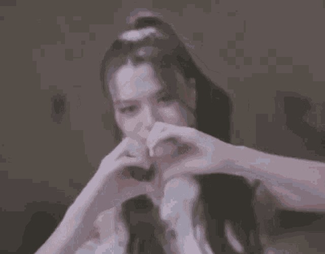 a woman is making a heart shape with her hands and looking at the camera .