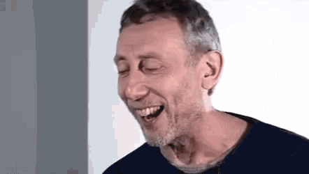 a man with a beard is laughing with his eyes closed while wearing a blue shirt .
