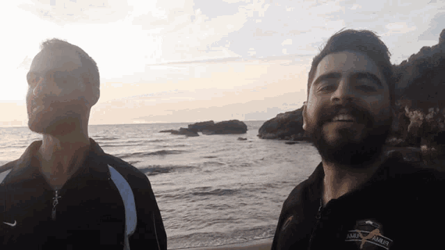 two men standing on a beach with one wearing a shirt that says ' mma armor '