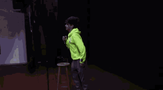 a person in a neon yellow hoodie stands in a dark room