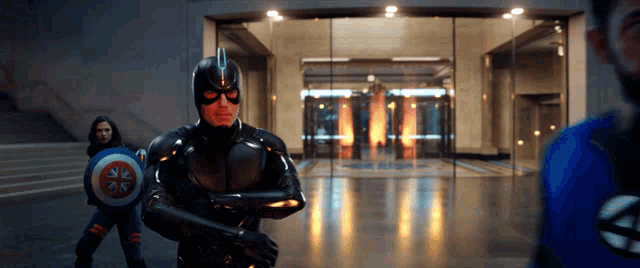 a man in a superhero costume is holding a shield in front of a glass door .