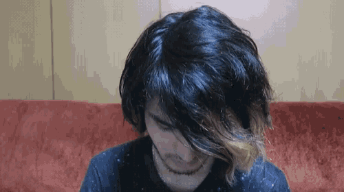 a man with long black hair is sitting on a red couch looking down .