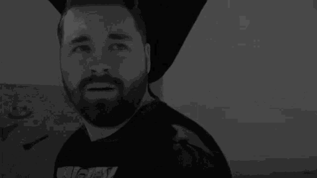 a man with a beard is wearing a black shirt and a black hat