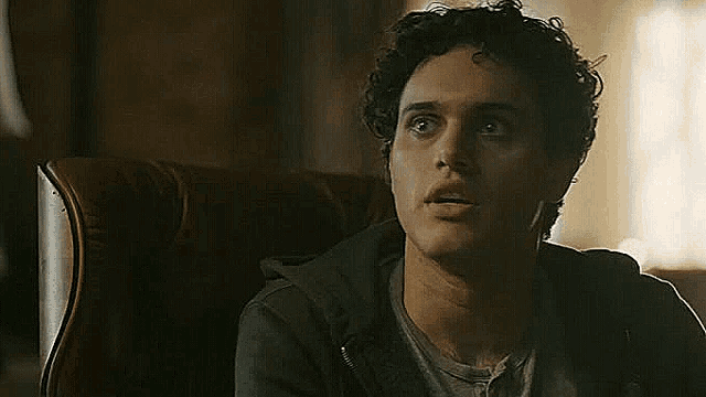 a young man with curly hair is sitting in a chair .