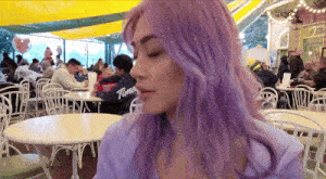 a woman with purple hair sits at a table in a restaurant