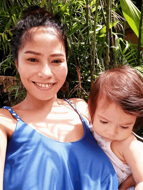 a woman in a blue tank top smiles while holding a baby