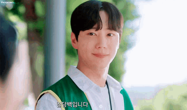 a young man wearing a green vest and white shirt is smiling and looking at the camera .