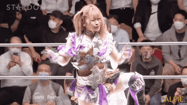a woman in a purple and white outfit is dancing in front of a crowd with the words stardom sports rus visible