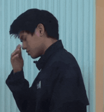 a man in a black jacket is blowing his nose with his hand .