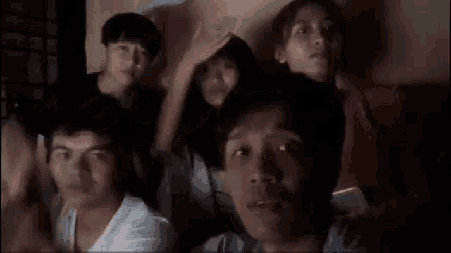 a group of people are sitting in a dark room with their hands on their head .