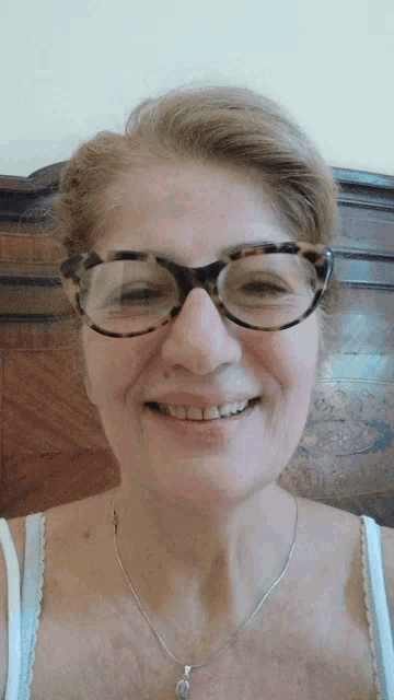 a woman wearing glasses and a necklace smiles at the camera