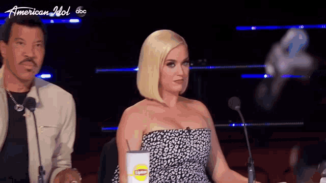 a woman in a strapless dress is sitting in front of a microphone with a cup of lipton tea .