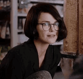 a woman wearing glasses and a black jacket is sitting in front of a cereal dispenser in a store .